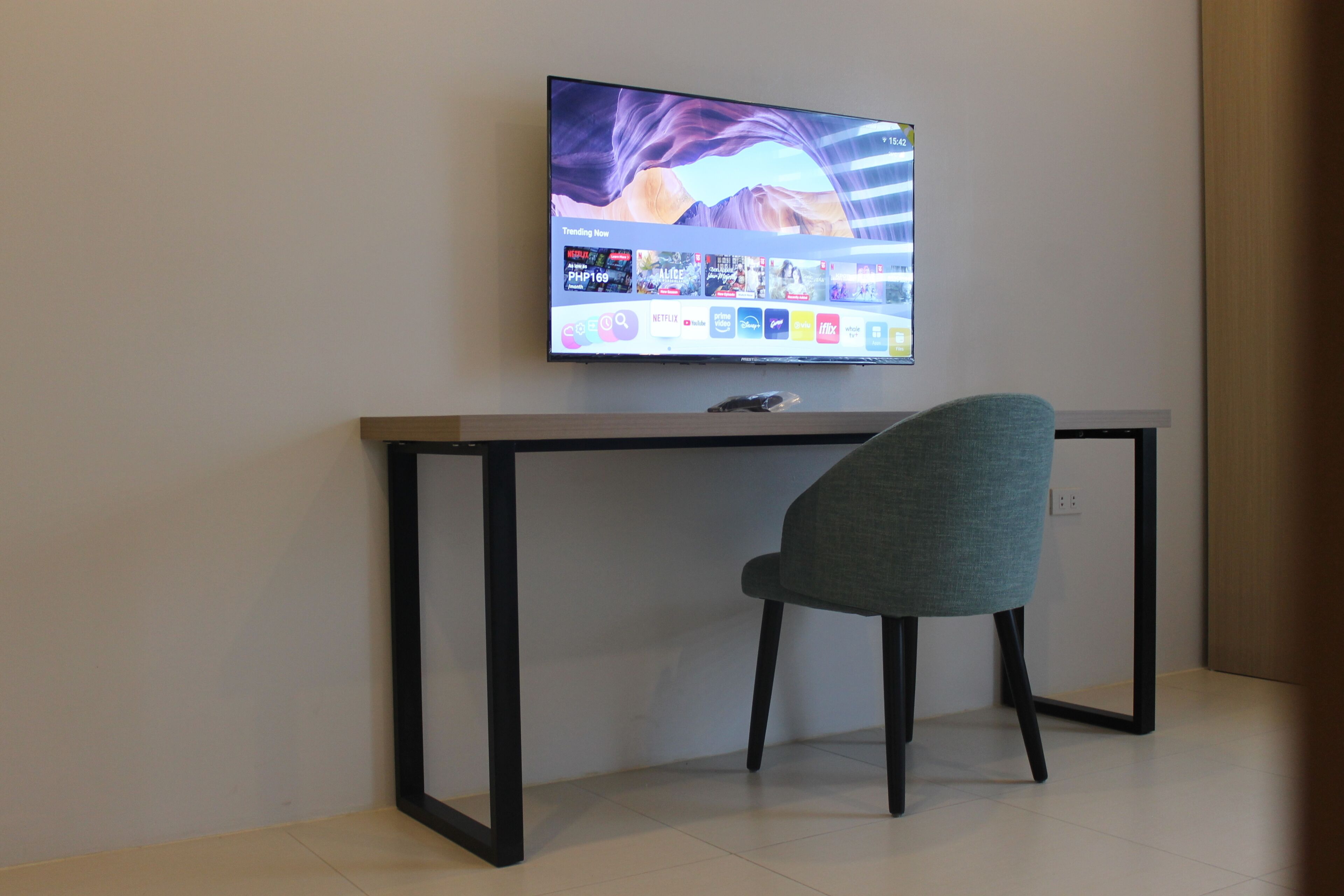 A modern room with a flat-screen TV mounted on the wall, a desk with a chair, and a tiled floor.