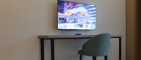 A modern room with a flat-screen TV mounted on the wall, a desk with a chair, and a tiled floor.