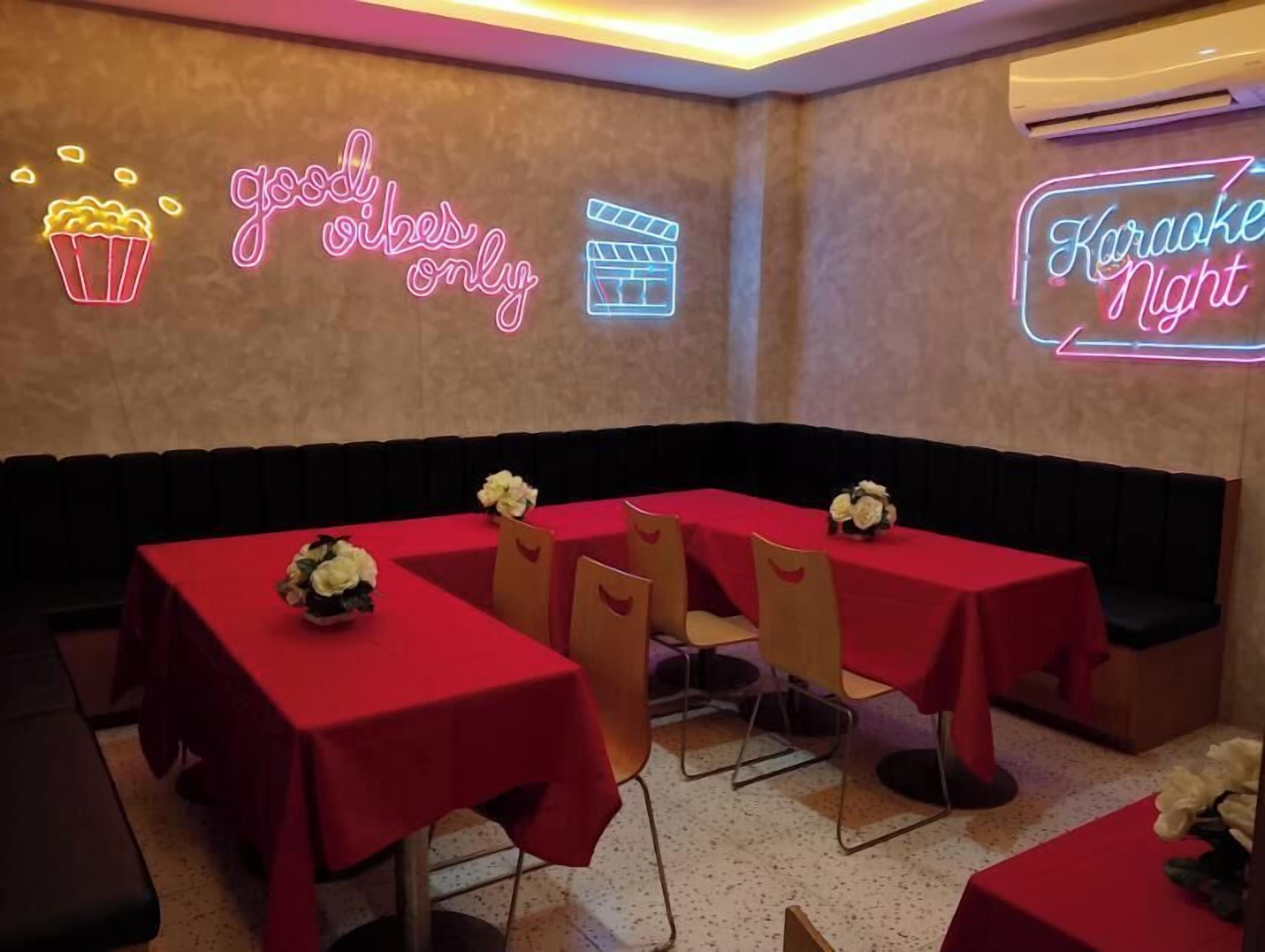 A room with tables covered in red tablecloths, neon signs reading "good vibes only" and "Karaoke Night", and a clapperboard sign.