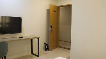A room with a TV on a stand, a desk, a chair, and a door with a number.