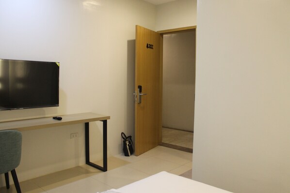 A room with a TV on a stand, a desk, a chair, and a door with a number.