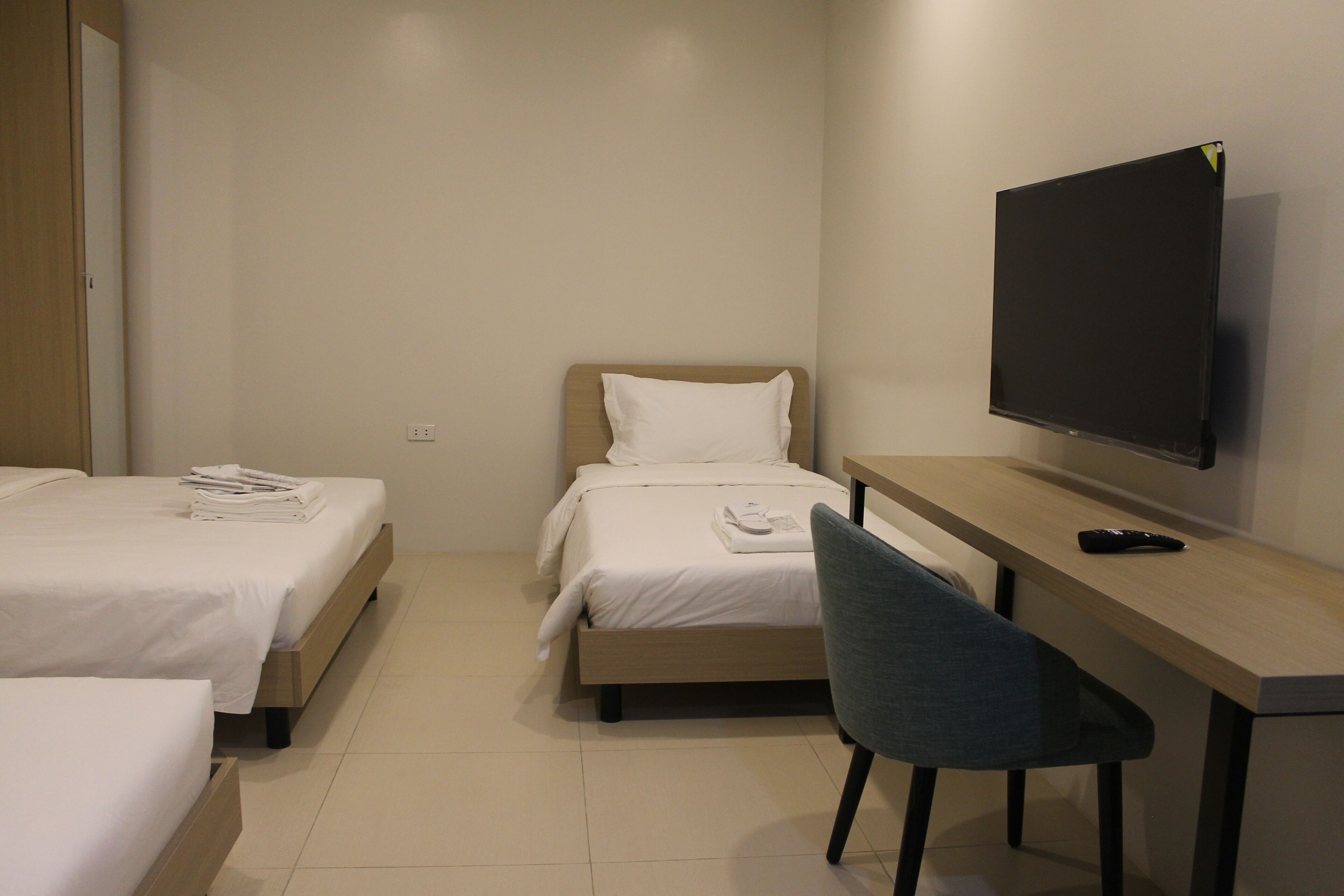 A hotel room with two beds, a desk, a chair, and a TV.