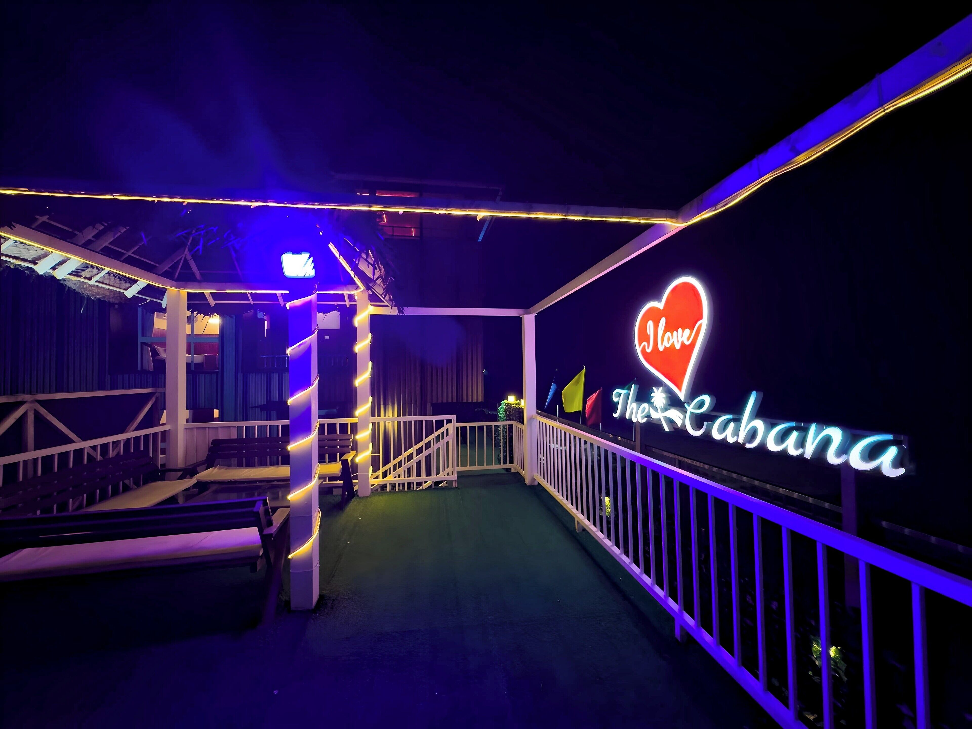 Ein überdachter Außenbereich mit einem Neonlichtschild, das 'I love The Cabana' zeigt.