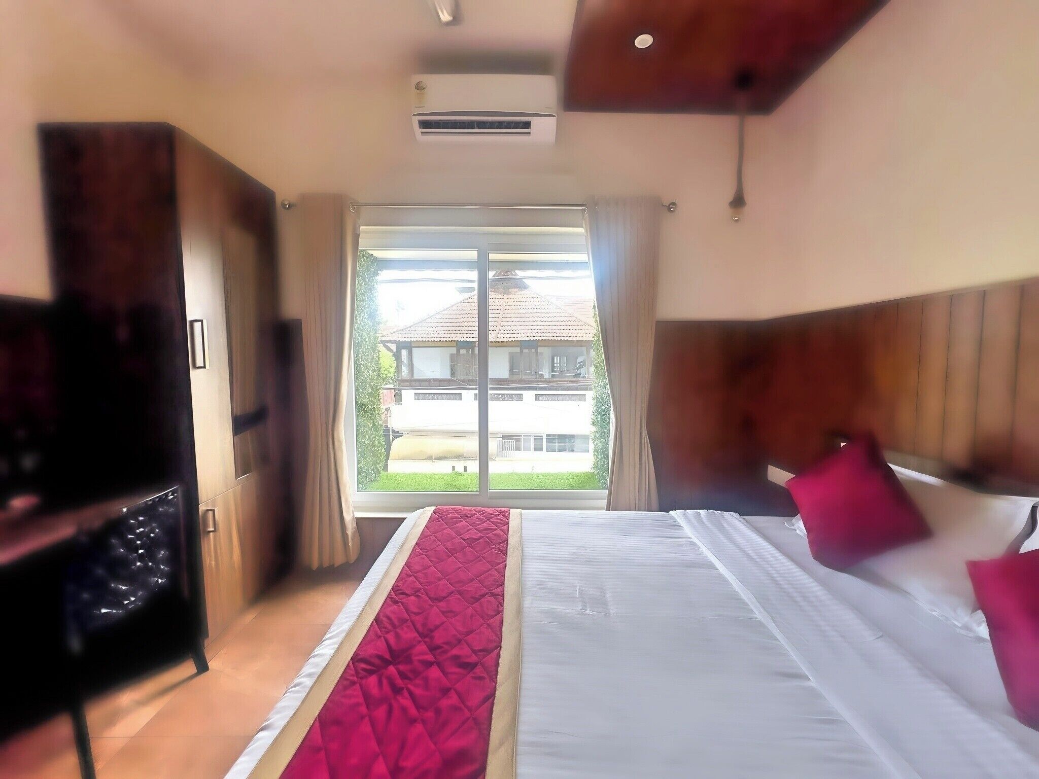 A hotel room with a bed, a TV, a window, and a view of a building outside.