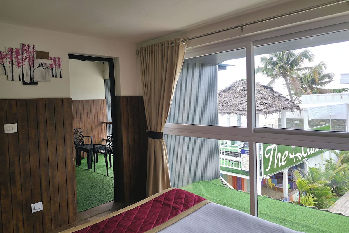 Ein Hotelzimmer mit Bett, einem Vorhangfenster, einer Holzvertäfelung und Blick auf einen Pool und Palmen.