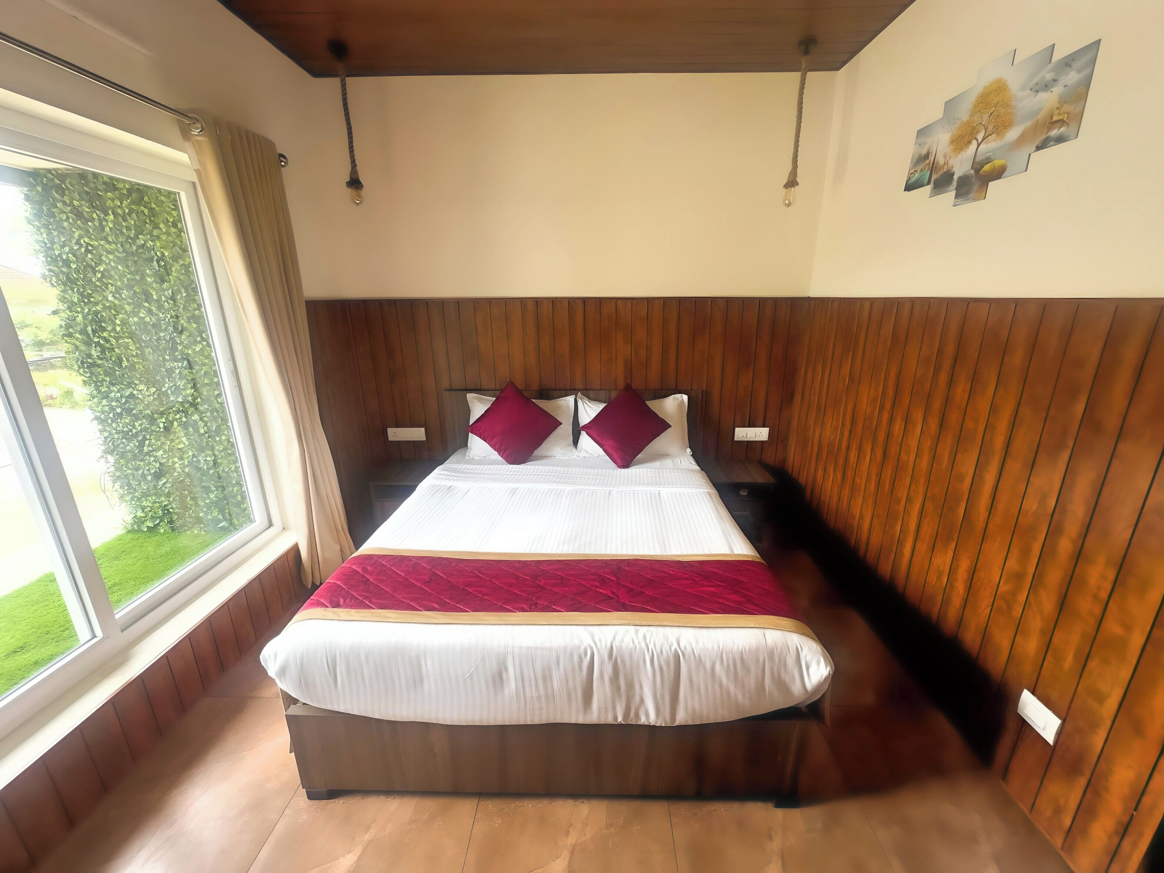 A hotel room with a large bed, wooden paneling on the walls, a window with curtains, and a painting on the wall.