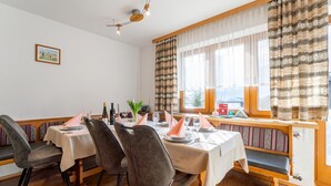 Ein Essbereich mit einem Tisch für vier Personen, Stühlen, einer Bank, einem Fenster mit Vorhängen und einem Bild an der Wand.