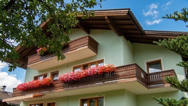Ein mehrstöckiges Gebäude mit Balkonen, die mit Blumen geschmückt sind, einem gepflegten Garten und blauem Himmel.