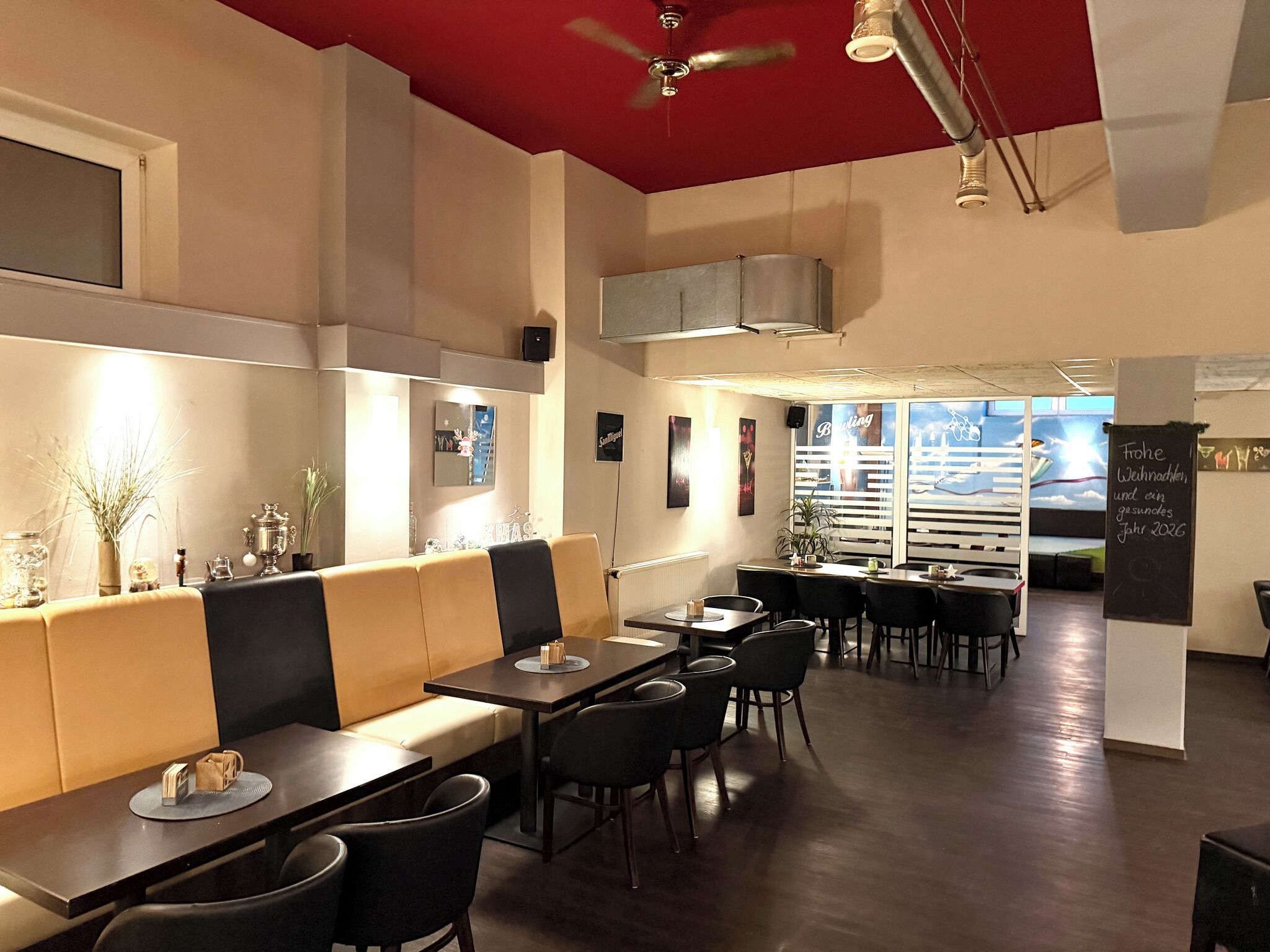 Un restaurante con mesas altas y cabinas, techo rojo y vistas de la ciudad a través de amplios ventanales.