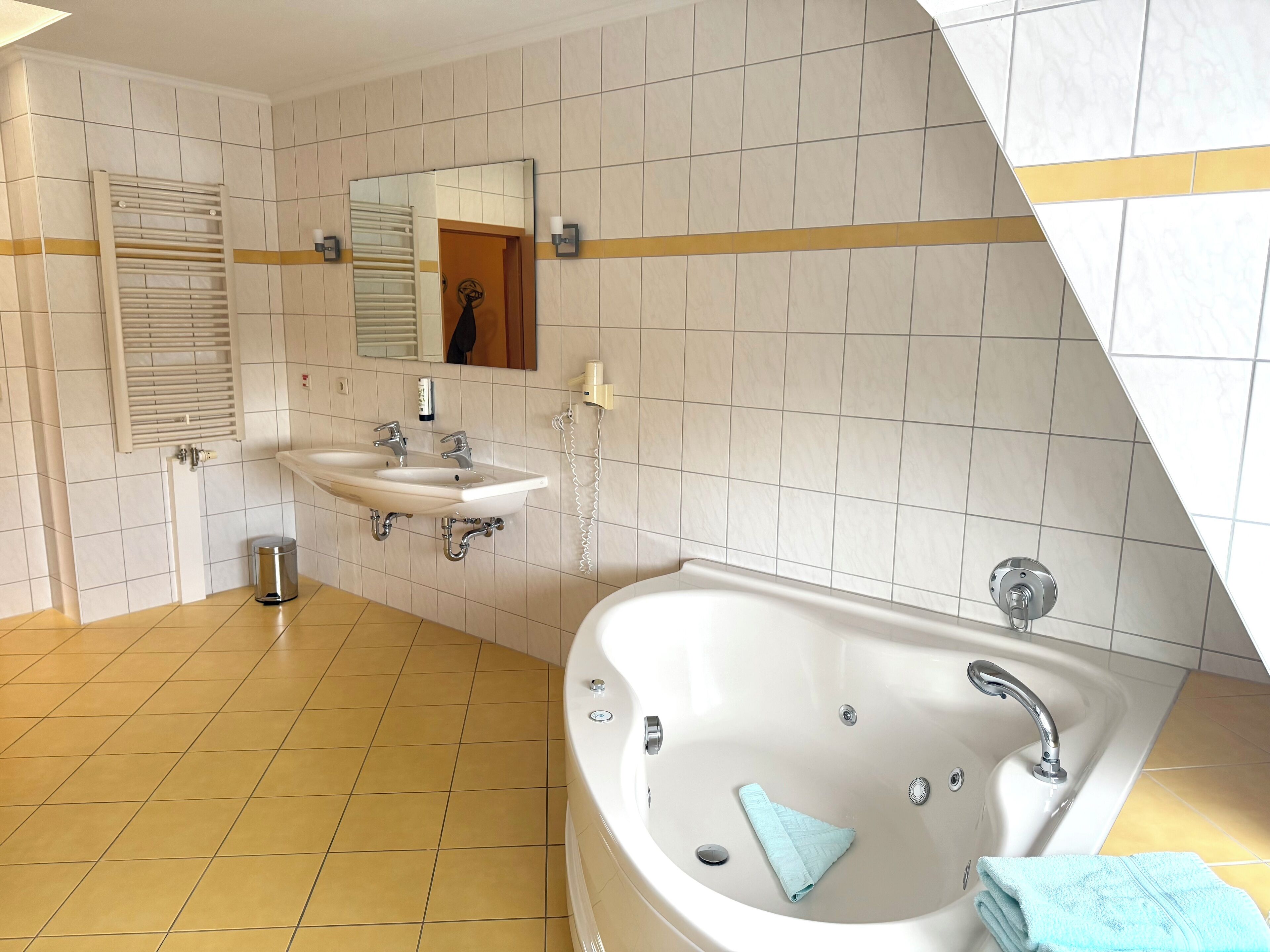 A modern bathroom with a bathtub, two sinks, a towel rack, and a mirror.