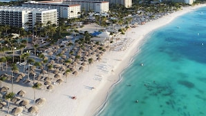 A beach resort with multiple hotel buildings, a sandy beach, and thatched umbrellas. - Oceanfront 10BR Lux Villa • Pool • Full Ocean View (Noord)