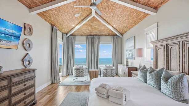 A bedroom with a wooden ceiling, a large bed with pillows, a dresser, and a view of the ocean. - LUX Family Teddy's Heaven - Beachfront - 6 Seater LSV - Pool-Hottub (Panama City Beach)