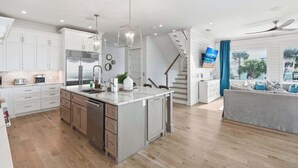 A modern kitchen with white cabinetry, a central island, and a dining area with a grey sofa. - LUX Family Teddy's Heaven - Beachfront - 6 Seater LSV - Pool-Hottub (Panama City Beach)