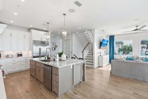 A modern kitchen with white cabinetry, a central island, and a dining area with a grey sofa. - LUX Family Teddy's Heaven - Beachfront - 6 Seater LSV - Pool-Hottub (Panama City Beach)