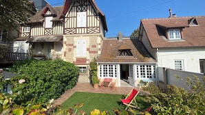 A traditional half-timbered house with a well-maintained garden, a red chair, and a small patio area. - Le Petit Shamrock - exceptional villa on the beach (Cabourg)