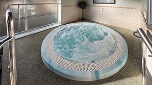 Een jacuzzi met betegelde vloer, een metalen leuning, een aan de muur hangend schilderij en een potplant.