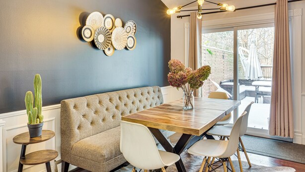 A dining area with a wooden table, white chairs, a tufted sofa, and a wall-mounted light fixture. - Faith-Based Retreat: Peace, Restoration, Healing (Berea)