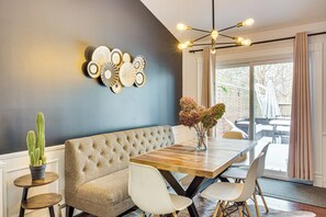 Un coin repas comprenant une table en bois, des chaises blanches, un canapé capitonné et un luminaire fixé au mur.