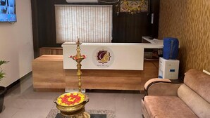 Una zona de recepción con mostrador, una lámpara decorativa, un arreglo floral y un televisor montado en la pared.