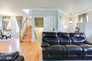 A spacious living area with a black leather sofa, wooden flooring, a staircase, and a dining area with a table and chairs. - 5 Mi to Show Place Arena: Quiet Townhome w/ Patio (Upper Marlboro)