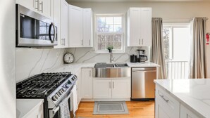 Una cocina moderna con armarios blancos, electrodomésticos de acero inoxidable, un reloj y una ventana con cortinas.