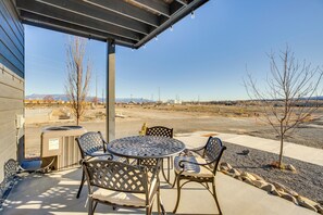 Un patio exterior con una mesa metálica redonda y cuatro sillas, una unidad de aire acondicionado pequeña y vistas a un paisaje lejano con montañas y un cielo despejado.