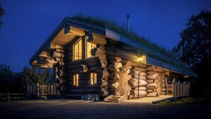 Une cabane en rondins avec un toit en pente, de grandes fenêtres et un porche à l’avant.