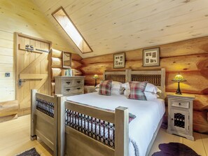 Een slaapkamer in een houten chalet, met een bed, nachtkastjes, een dressoir, een spiegel en een dakvenster.