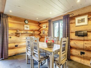 Een houten interieur met een eettafel, stoelen, een klok, ingelijste foto's en een televisie.