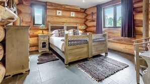 A log cabin bedroom with a wooden bed, bedside tables, a rug, and a window with curtains. - 3 bedroom accommodation in Beauly, near Drumnadrochit (Beauly, near Drumnadrochit)