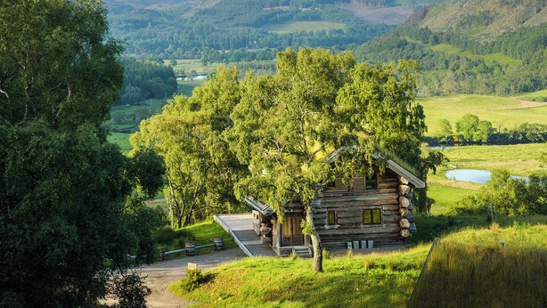 A log cabin with a porch, surrounded by lush greenery and hills. - 3 bedroom accommodation in Beauly, near Drumnadrochit (Beauly, near Drumnadrochit)