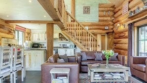 A log cabin interior with a wooden staircase, a living area with a sofa and coffee table, and a kitchen in the background. - 3 bedroom accommodation in Beauly, near Drumnadrochit (Beauly, near Drumnadrochit)