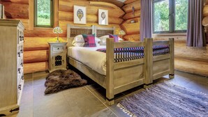 Un dormitorio tipo cabaña de madera con cama, mesita de noche, cómoda y ventana con cortinas.