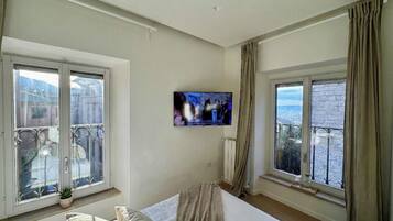 Habitación de hotel con cama, televisor montado en la pared y grandes ventanas con vistas a la ciudad.