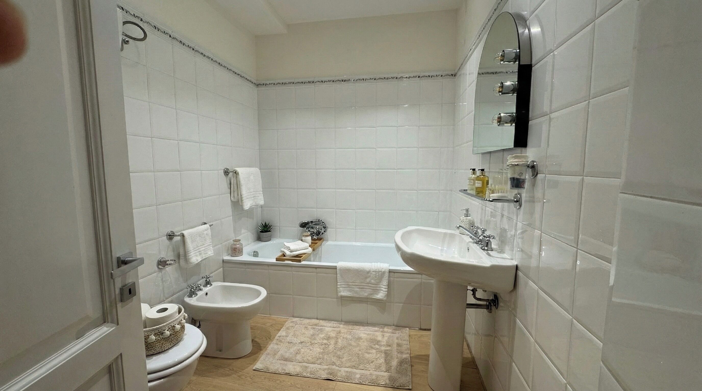 A bathroom with white tiles, a bathtub, a sink, a bidet, and a toilet.