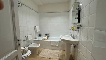 A bathroom with white tiles, a bathtub, a sink, a bidet, and a toilet.