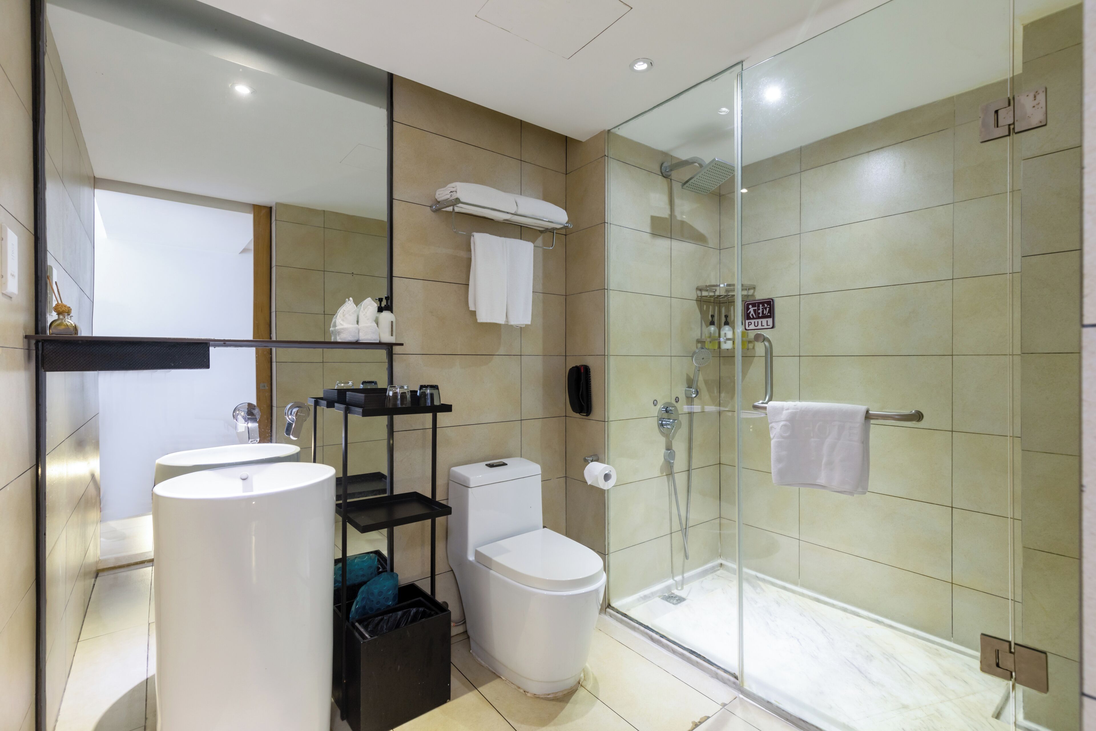 A modern bathroom with a glass-enclosed shower, two sinks, a toilet, and a towel rack.