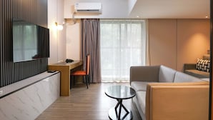 Une chambre d’hôtel moderne équipée d’un téléviseur à écran plat, d’un bureau, d’une chaise, d’un canapé et d’une petite table.