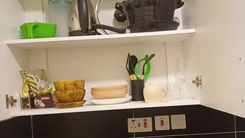 Een keuken met een spoelbak, fornuis en aanrecht. Er staan diverse keukenbenodigdheden in de kastjes, zoals een groene mand, een zwarte pan en een houten snijplank.