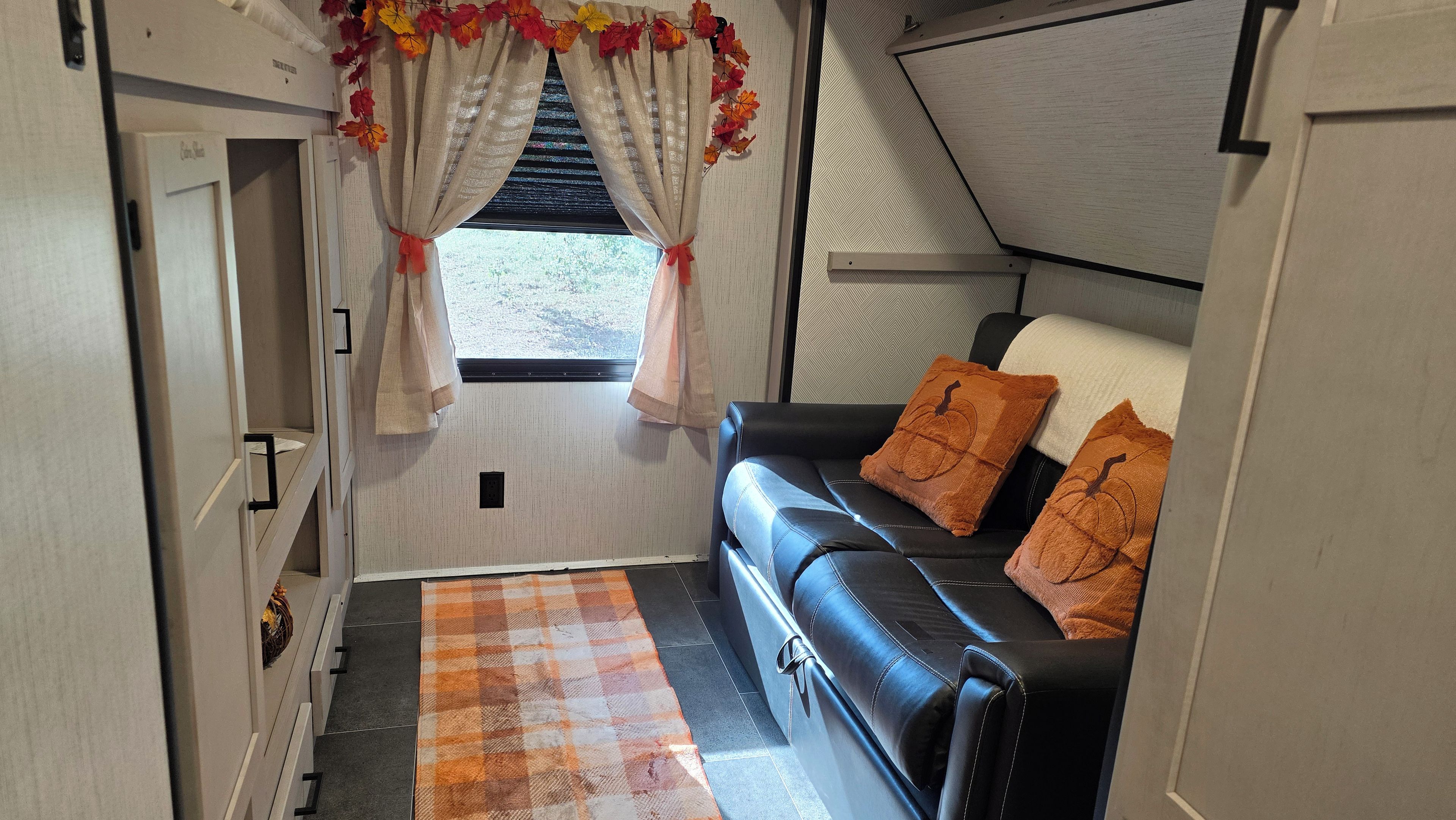 A compact living space with a sofa, decorative pillows, a checkered rug, and curtains with autumn leaves.