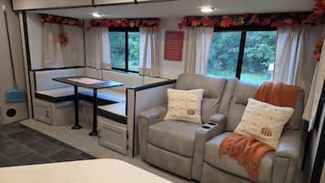 A cozy RV interior with a seating area, a table, and a window with curtains.