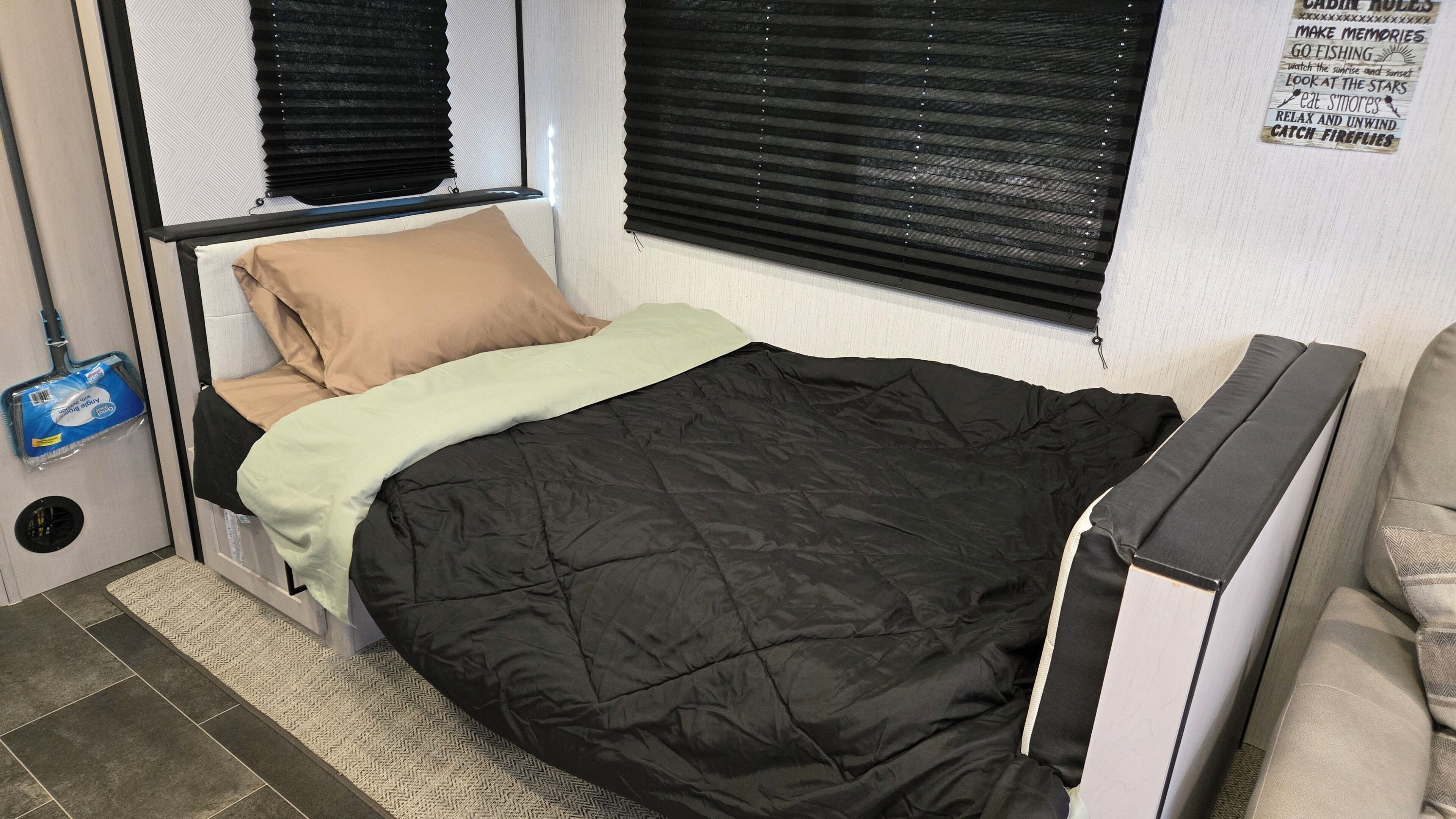 A compact bed with a black and white headboard, a beige pillow, and a light green blanket.