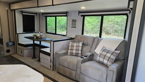 Een gezellig interieur van een camper, met een eethoek, een zachte zithoek en grote ramen met uitzicht op groen.