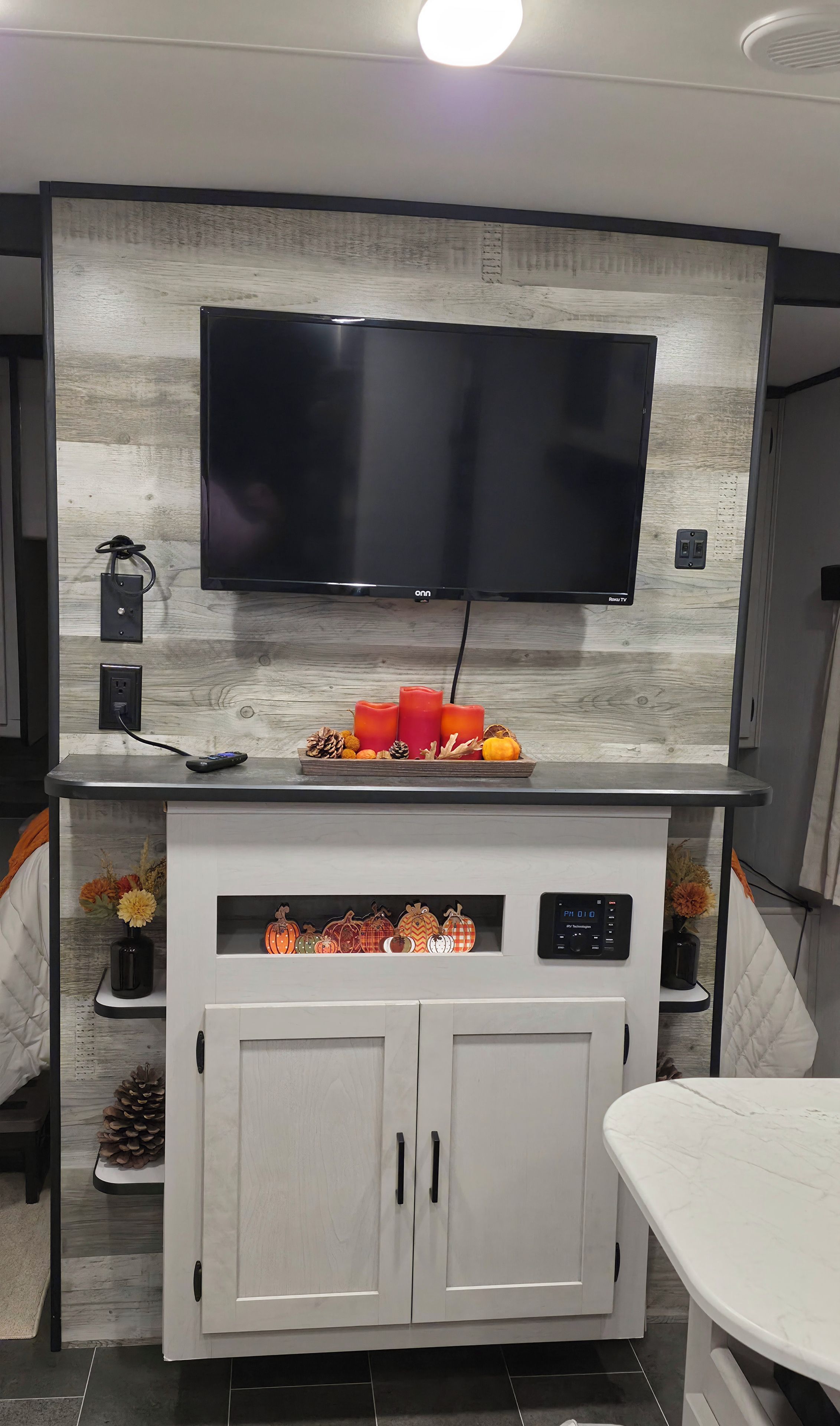 A modern kitchen with a flat-screen TV mounted on a wooden backsplash, a built-in oven, and a dining area with a white table.