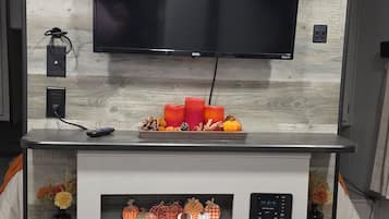 A modern kitchen with a flat-screen TV mounted on a wooden backsplash, a built-in oven, and a dining area with a white table.