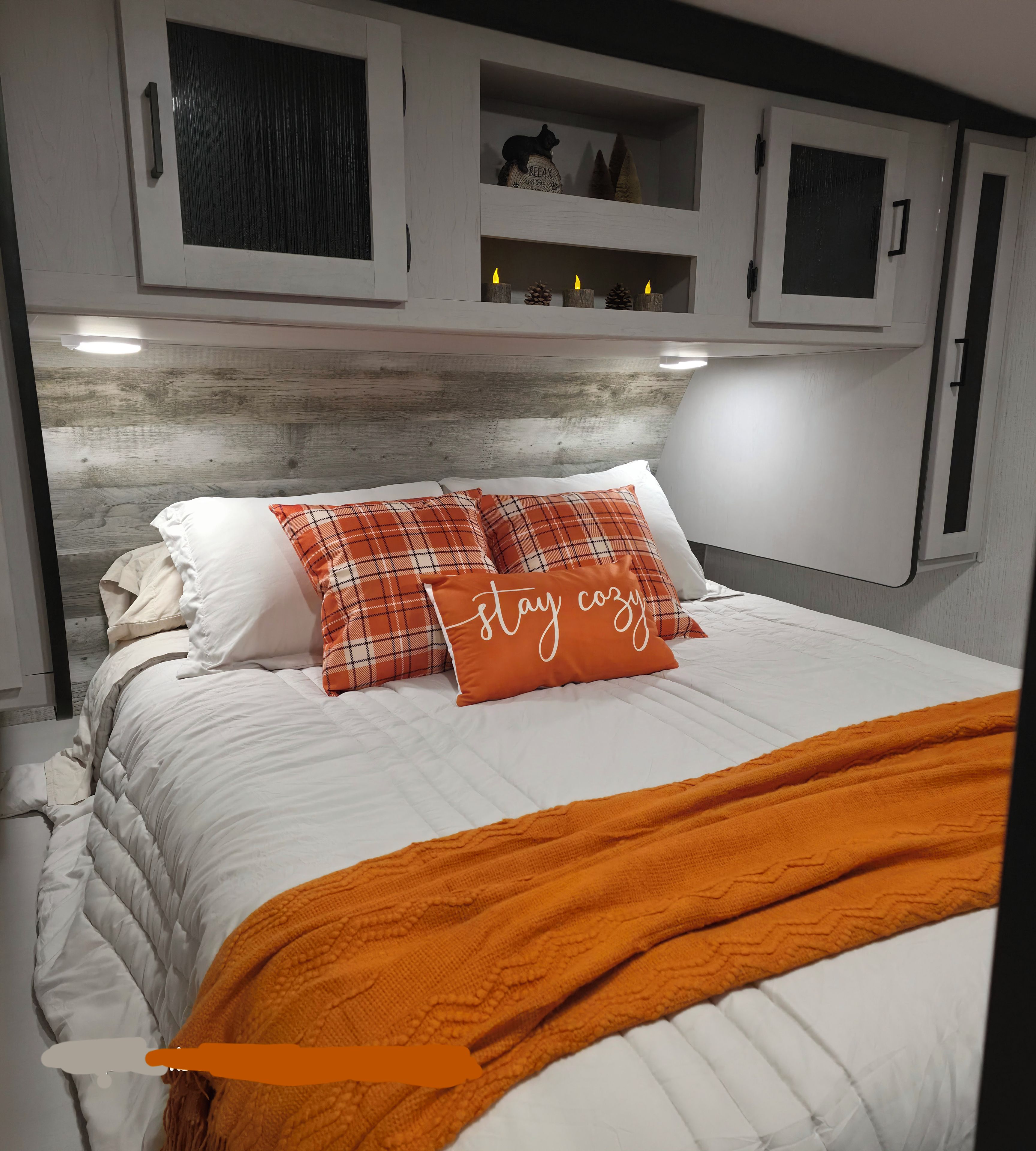 A bed with white bedding, orange and white pillows, and a 'stay cozy' pillow.