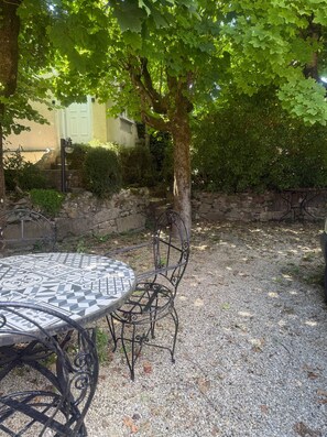 A patio area with a round table and chairs, surrounded by gravel and trees.
