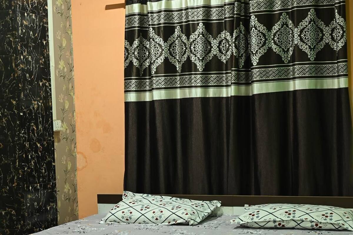 A bedroom with a bed, floral bedspread, patterned curtains, and a wall with a floral wallpaper design.