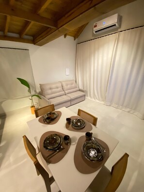 A dining area with a table set for four, a sofa, and an air conditioning unit. - Pitanga House - Ponta do Papagaio Beach (Palhoça)