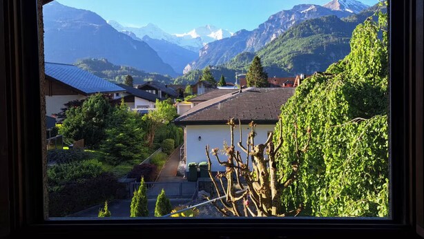 Un village de montagne avec des maisons, un ciel dégagé et, au loin, des sommets enneigés.